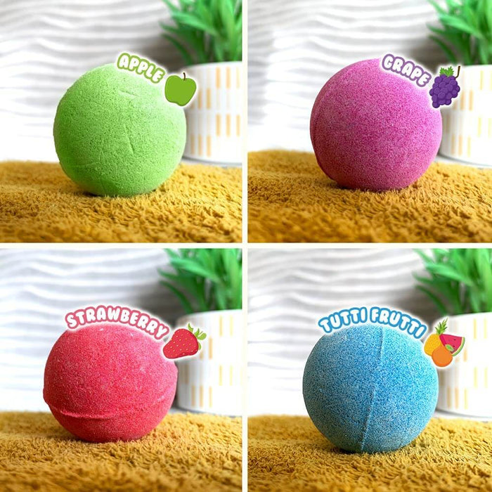 Green, purple, red, and blue round bath bombs labeled Apple, Grape, Strawberry, and Tutti Frutti on a yellow towel.