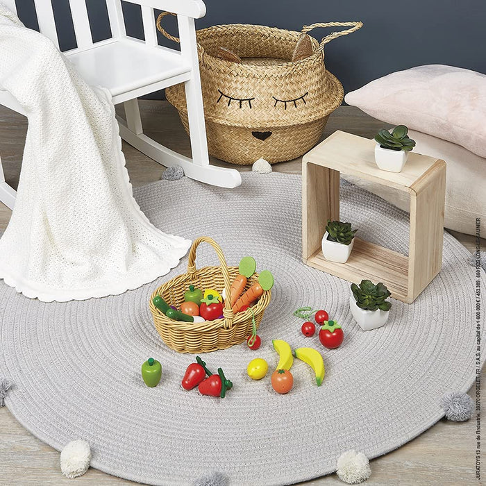 Woven toy basket with a variety of colorful wooden play fruits and vegetables on a round grey braided rug.