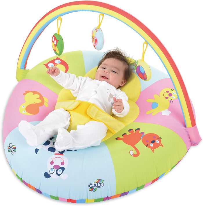 Baby in a colorful, circular Galt playnest with animal prints and a rainbow toy arch with hanging soft toys.