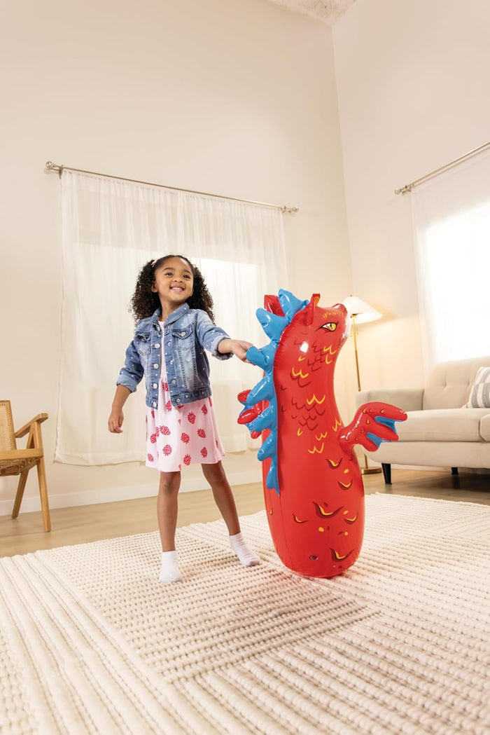Young girl playing with a red inflatable dragon bop bag featuring blue spikes and yellow details in a living room.