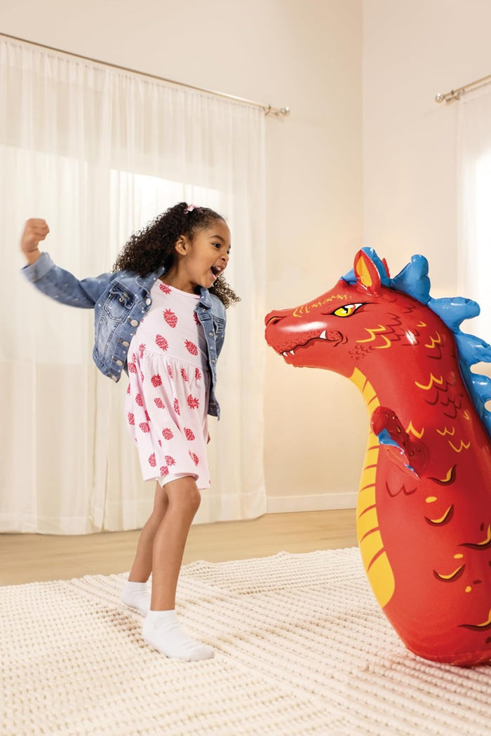 Young girl with fist raised playing with a large red inflatable dragon bop bag.