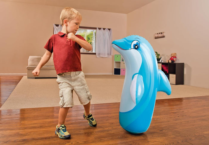 Young boy punches a blue dolphin-shaped inflatable bop bag toy standing in a living room.