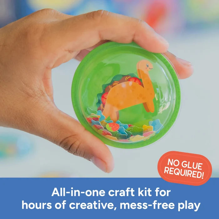 Hand holding a round, clear 3D sticker dome with an orange dinosaur and colorful confetti inside.