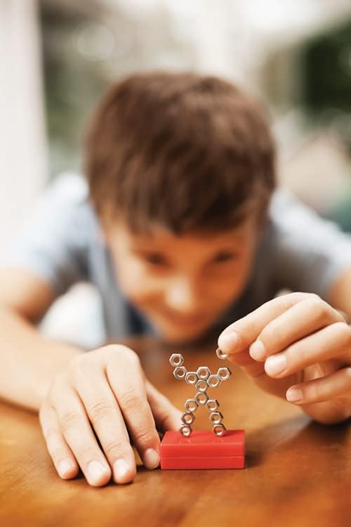 A child builds a figure using small metal nuts on a red rectangular magnet base.