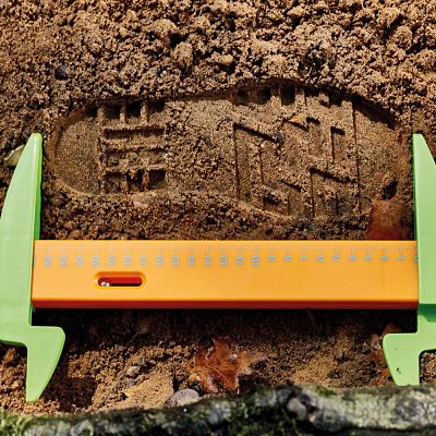 Bright orange ruler with green calipers measuring a boot print in brown soil.