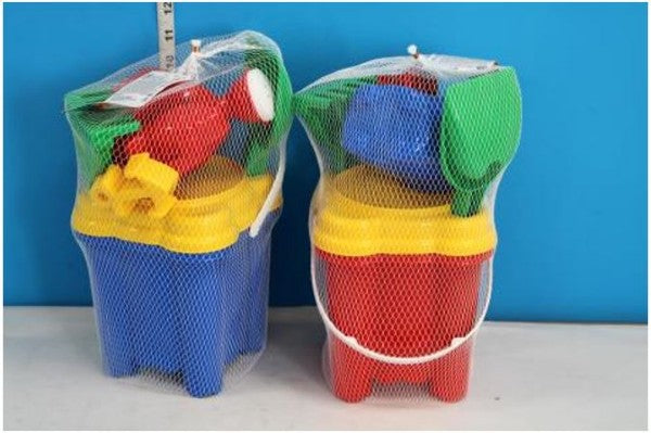 Red and blue castle-shaped beach buckets with yellow lids and colorful toy tools packaged in white mesh bags.