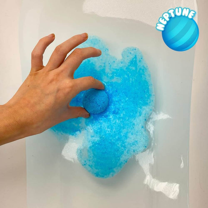 Hand placing a blue Neptune bath bomb into water, creating a vibrant blue cloud of fizz and foam.