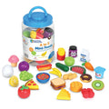 Clear plastic jar with blue lid surrounded by colorful toy food miniatures of fruits, vegetables, and snacks.