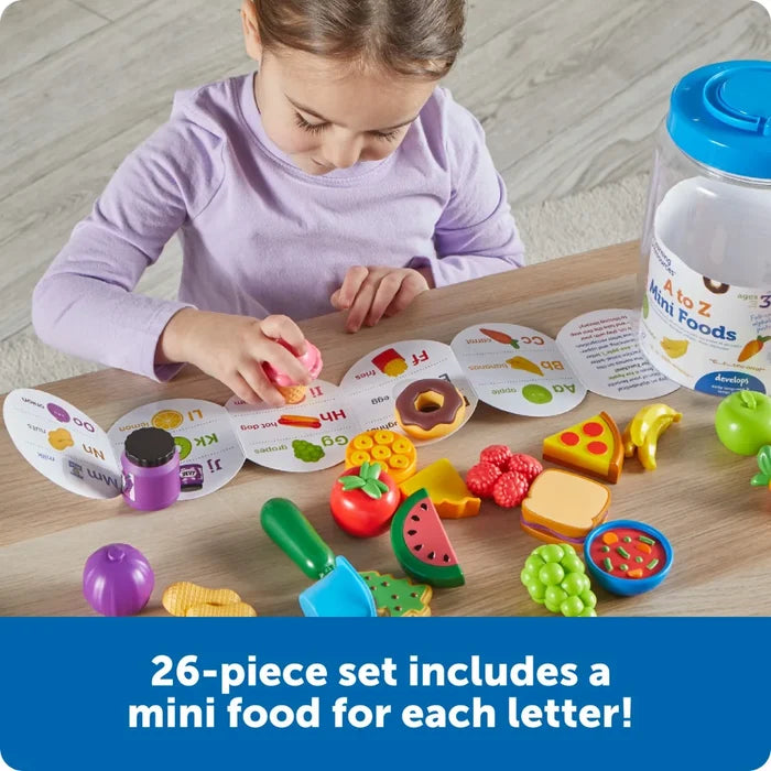 Child plays with colorful plastic food toys and an alphabet guide next to a clear storage jar on a wooden table.