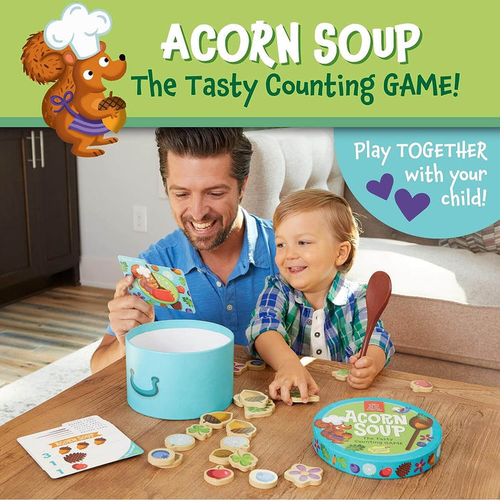 Father and toddler play Acorn Soup game with a blue pot, wooden ingredient discs, and a wooden spoon on a table.