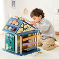 Child playing with a wooden activity house featuring colorful gears, shape sorters, and a ball ramp on a white rug.