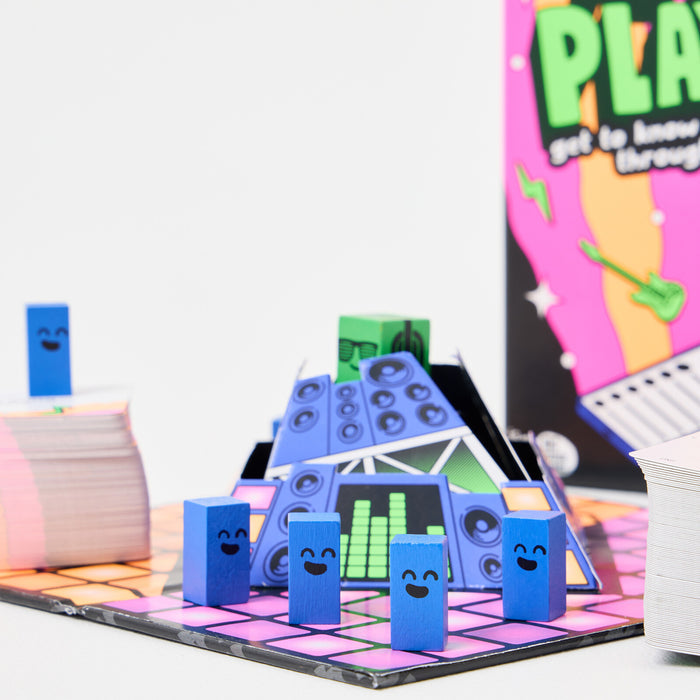 Blue smiley blocks and a green block with headphones on a checkered game board with a cardboard DJ booth and cards.
