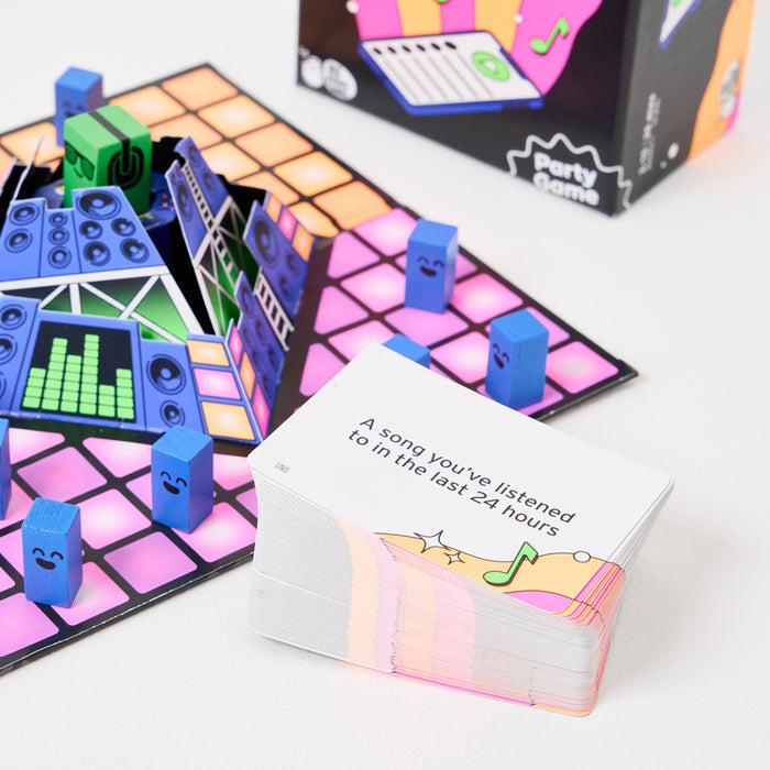 Music party game board with 3D speaker center, blue character tokens, and a deck of song-themed prompt cards.