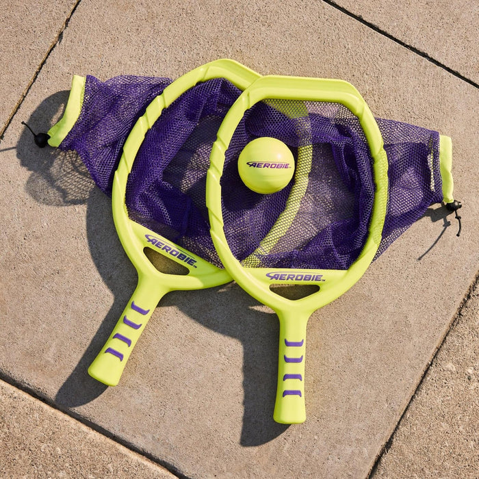 Two neon yellow paddles with purple mesh nets and a yellow ball on a concrete surface.