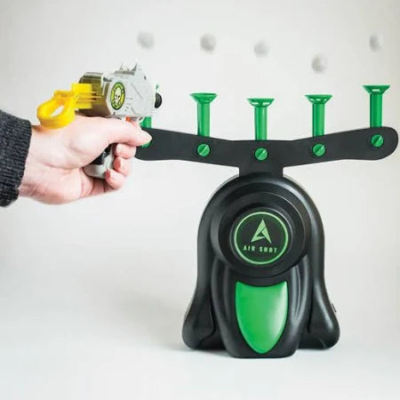 Hand aiming a toy blaster at white foam balls hovering above green nozzles on a black and green air-powered target base.