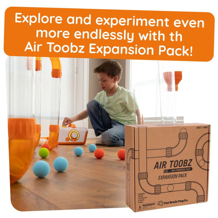 Child plays with clear tubes and colorful balls next to a brown cardboard box featuring black pipe illustrations.