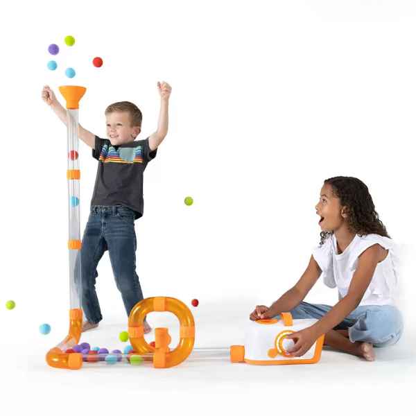Children play with clear tubes and a loop track, launching colorful foam balls from a white and orange blower base.