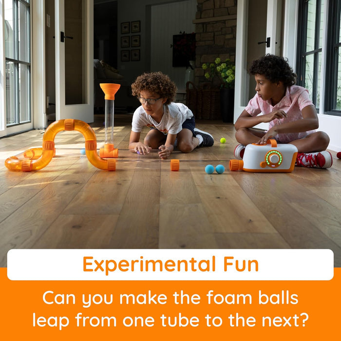 Two children playing with an air-powered toy set of orange tubes, a white blower, and colorful foam balls.