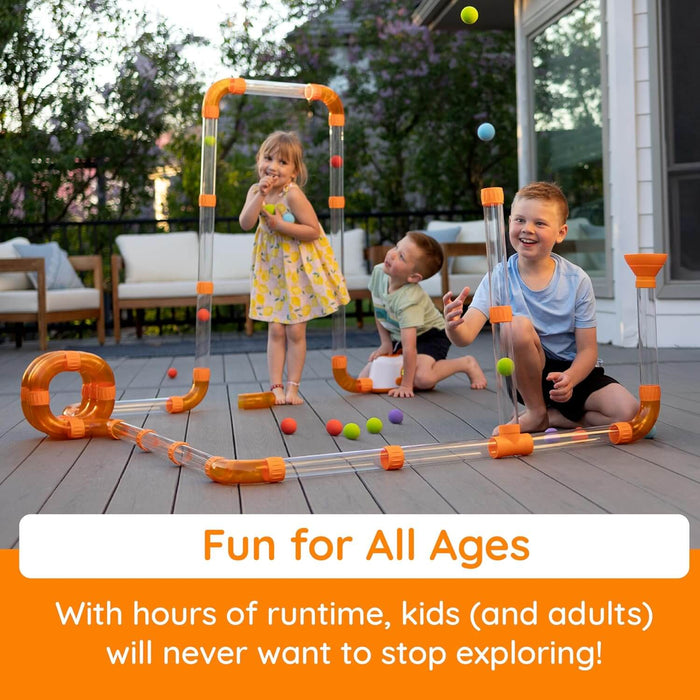 Three children playing with a clear and orange tube track that launches colorful balls into the air on a wooden deck.