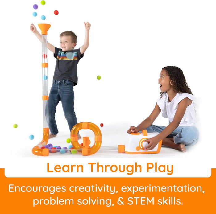 Two children using an air-powered clear tube system with orange joints to launch colorful balls through a loop tower.