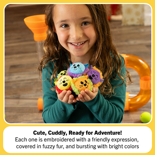 Smiling child holds five colorful, fuzzy plush balls with friendly embroidered animal faces in her cupped hands.
