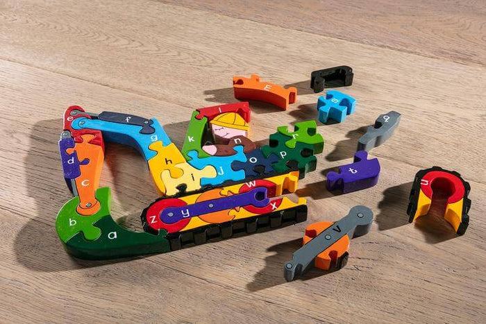 Colorful wooden puzzle pieces with lowercase letters forming an excavator, scattered on a light wood floor.