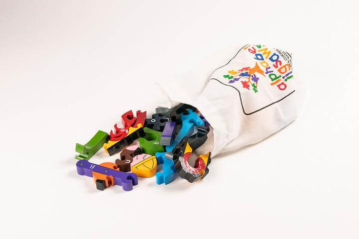 Colorful wooden puzzle pieces spilling from a white cotton bag with the Alphabet Jigsaw logo.