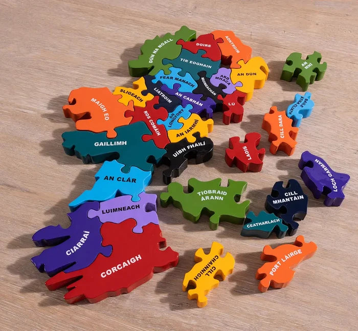 Colorful wooden map of Ireland puzzle with chunky county pieces labeled in Irish, some detached on a wood surface.
