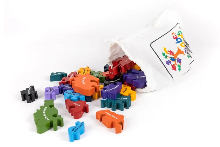 Colorful chunky wooden jigsaw pieces with Irish county names spilling from a white drawstring bag.