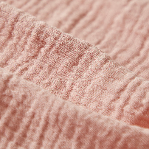 Close-up of soft, crinkled blush pink muslin fabric with a textured weave.