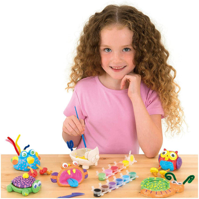 A young girl paints a clay animal surrounded by colorful finished figurines like an owl, turtle, and fish.