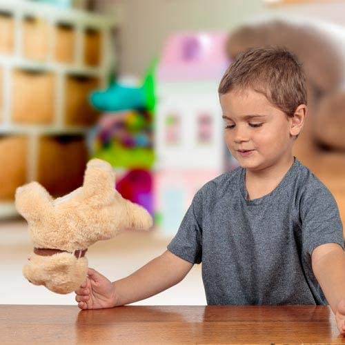 A small tan plush puppy performing a backflip in mid-air as a smiling young boy watches at a wooden table.