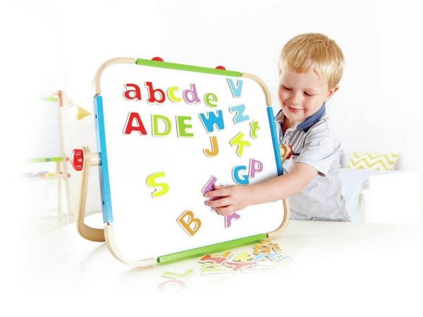 Child playing with colorful magnetic letters on a tabletop whiteboard with a natural wood frame and blue trim.