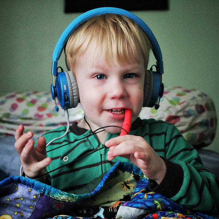 A young boy with blue headphones chewing on a red, textured saber-shaped sensory chew pendant.