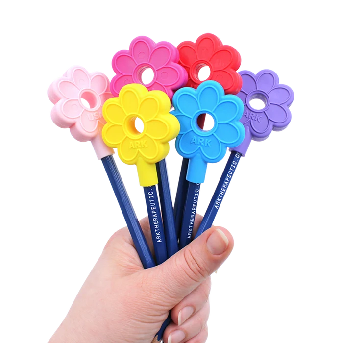 Six colorful flower-shaped silicone pencil toppers in pink, yellow, blue, red, and purple held in a hand.
