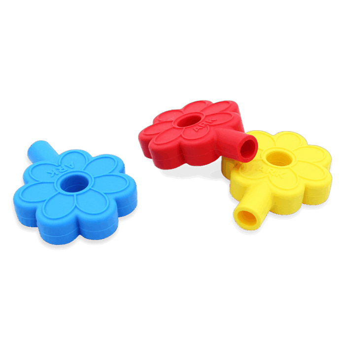 Three rubbery daisy-shaped toppers in blue, red, and yellow with central holes and the word ARK embossed on the petals.