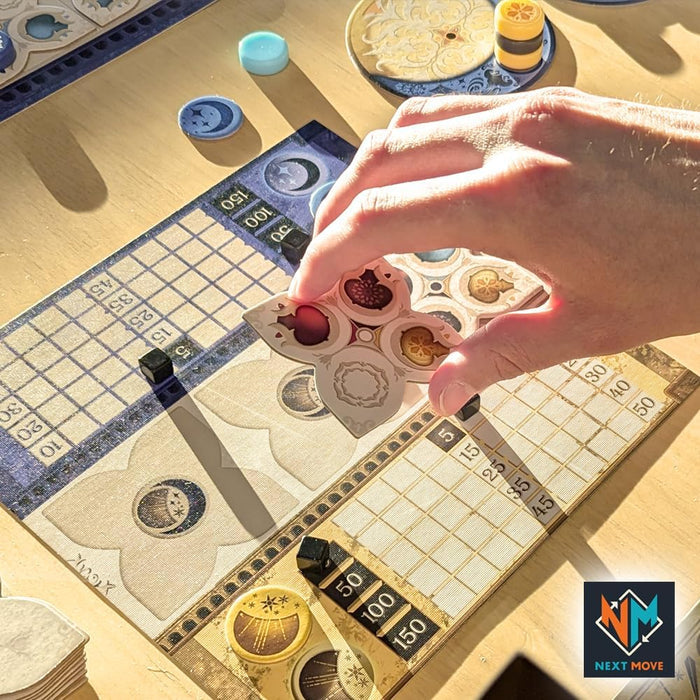 Hand placing a quatrefoil tile with colored icons on a grid board with blue tokens and sun and moon designs.