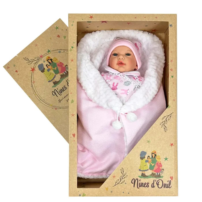 Realistic baby doll in a pink hat swaddled in a white fleece-lined pink blanket inside a branded cardboard gift box.