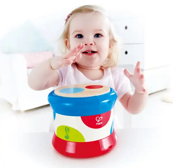 Smiling toddler playing with a blue, white and red toy drum with colorful spots and a wooden top.