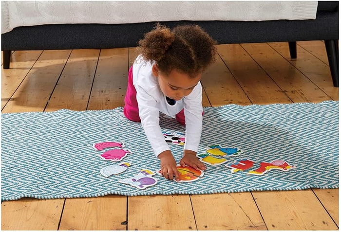 Toddler sitting on a blue rug plays with colorful animal-shaped puzzle pieces on a light wood floor.