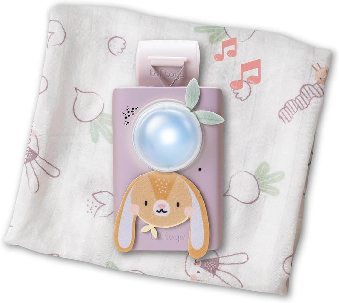 Purple bunny sound machine with a glowing blue light resting on a white bunny-patterned swaddle blanket.