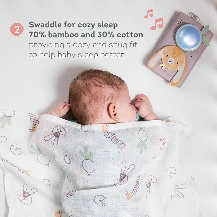 Sleeping baby swaddled in a patterned wrap next to a pink bunny sound machine with a glowing blue dome.