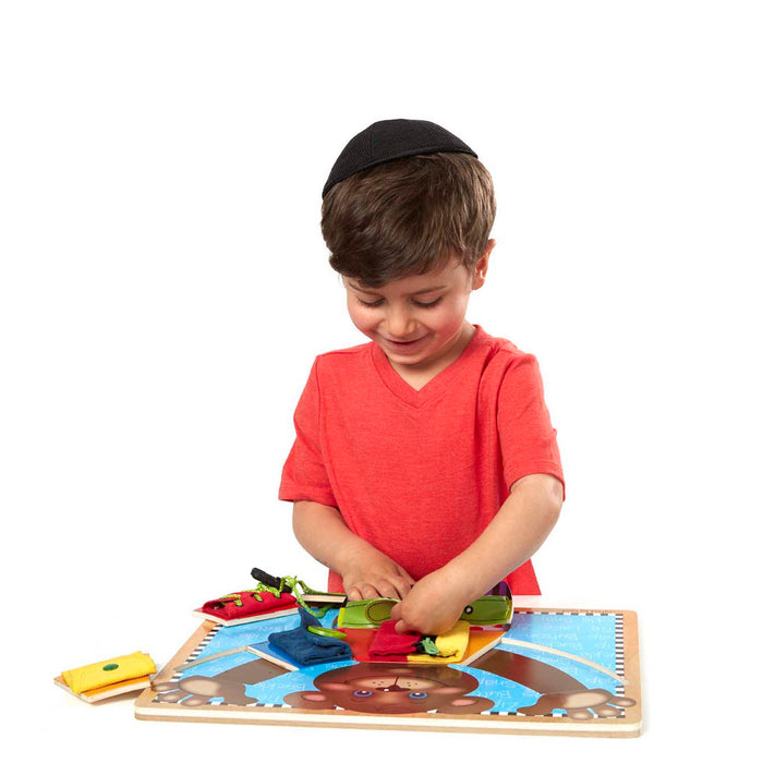 Boy using a wooden bear-themed puzzle board to practice fastening colorful fabric pieces with buttons and laces.