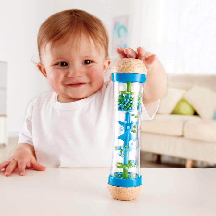 Baby touching a tall clear rattle with blue and green beads, blue internal wheels, and wooden end caps.