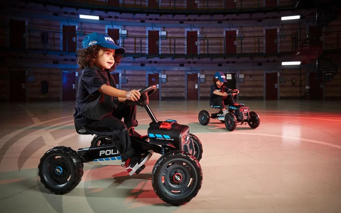 Children ride black pedal go-karts with chunky tires, siren lights, and police graphics in a circular indoor arena.