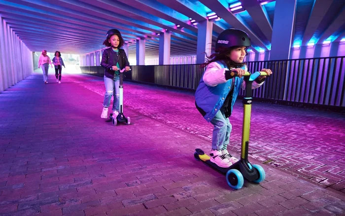 Girl riding a mint green 3-wheel kick scooter with glowing blue LED wheels through a vibrant neon-lit tunnel.