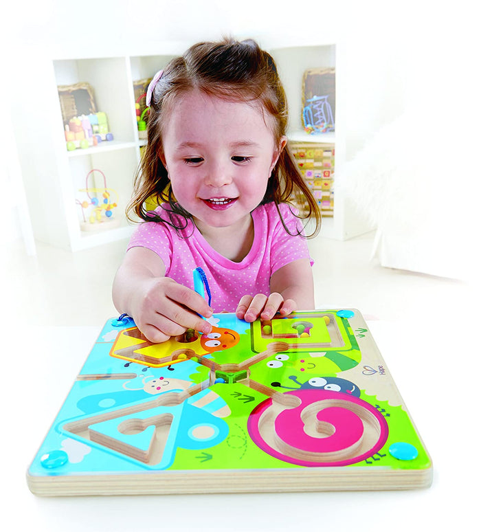 Young girl using a magnetic wand to guide colorful beads through an insect-themed wooden maze with geometric paths.
