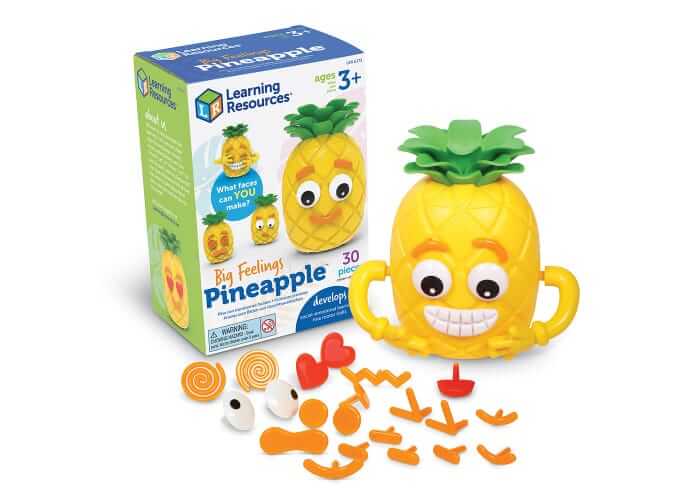Yellow pineapple toy with green leaves and a toothy grin, shown with its box and colorful facial feature pieces.