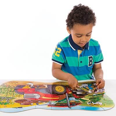 A young boy assembling a large floor puzzle featuring a bright red tractor and colorful farm scene.