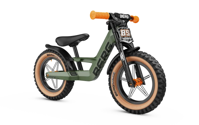 Olive green balance bike with chunky off-road tires, tan sidewalls, and orange handlebar grips.